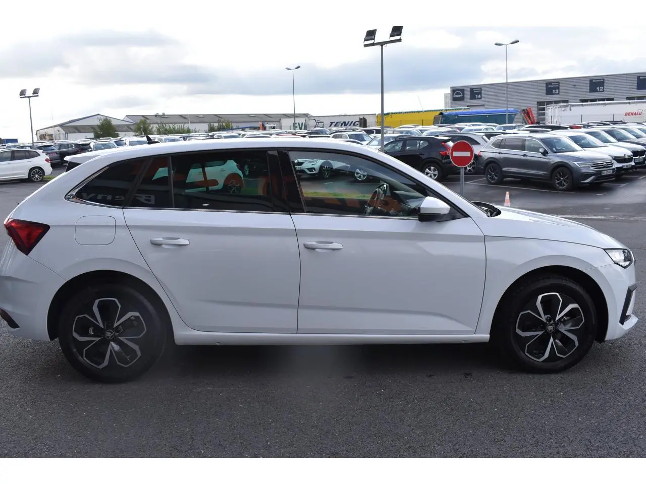 Vue latérale droite d'une Skoda Scala blanc glacier avec jantes alliage noires et détails modernes sur parking.