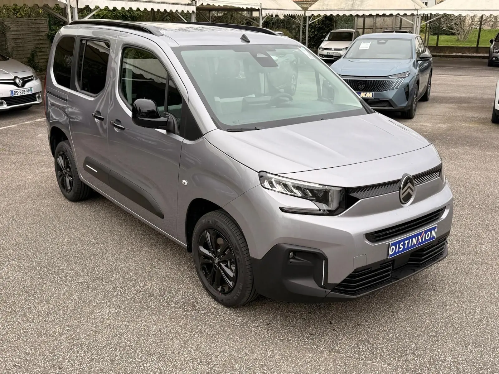 Vue 3/4 avant droit du Citroën Berlingo gris Artense 2025 avec jantes noires et calandre moderne sur parking.