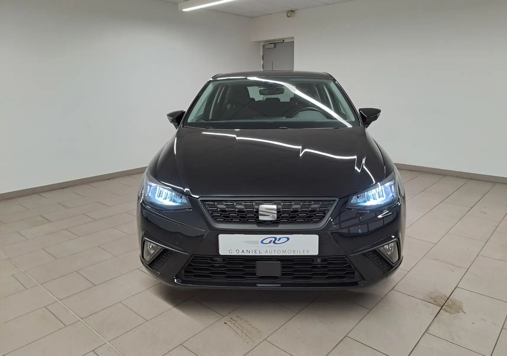 Vue avant d'une SEAT Ibiza 2024 noir minuit avec phares LED allumés dans un showroom lumineux.