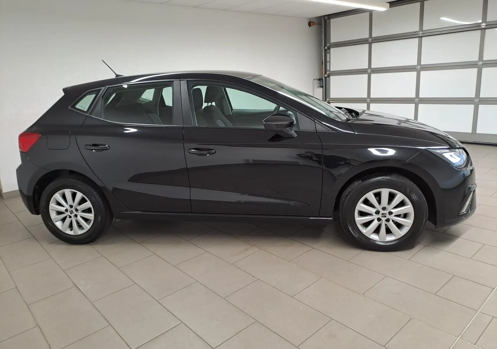 Profil droit d'une SEAT Ibiza 2024 noir minuit, avec jantes alliage et phares allumés dans un garage.