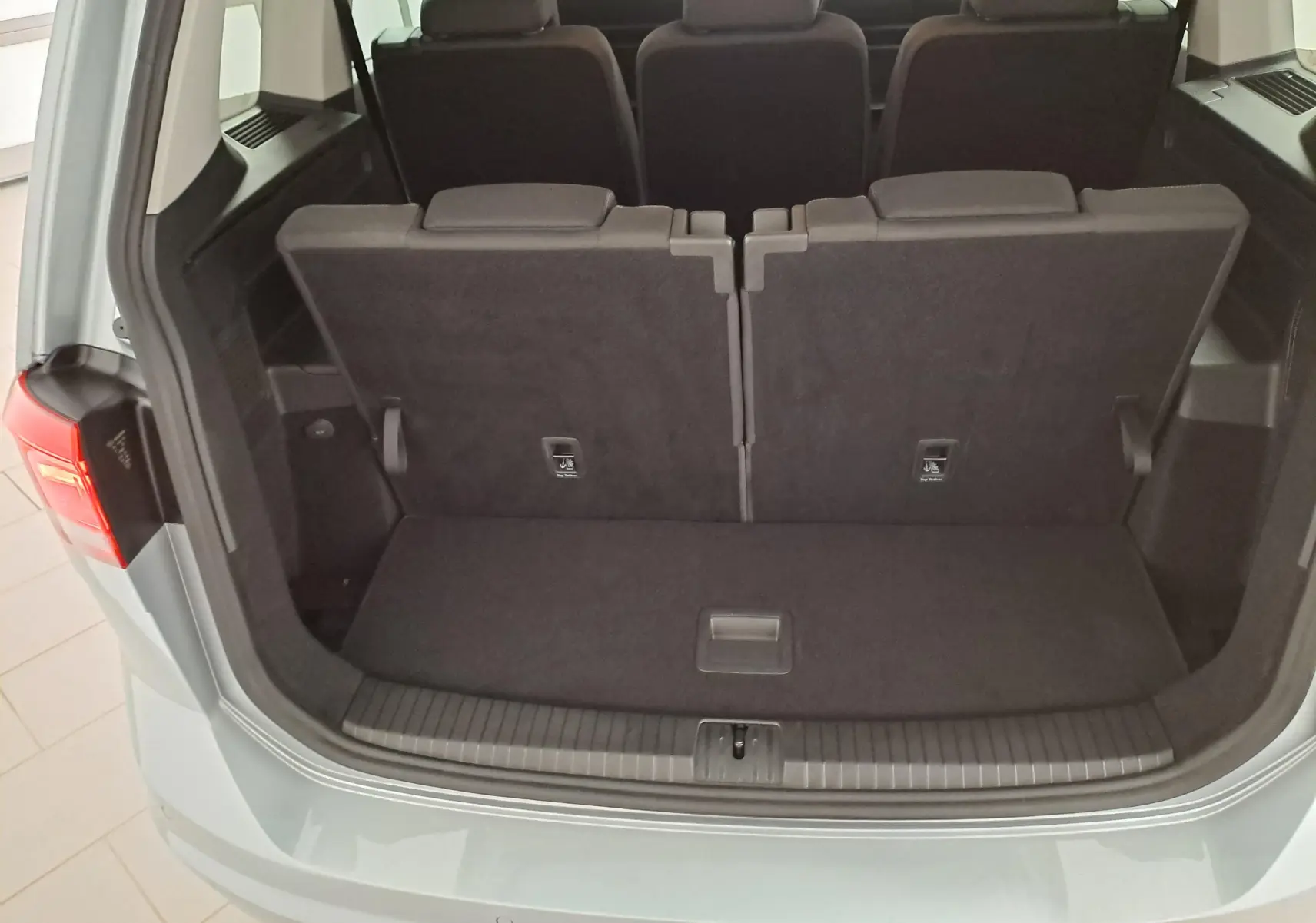 Vue arrière du coffre ouvert du Volkswagen Touran 2025 en Argent Dolomite, montrant les sièges arrière repliés et l'espace de chargement.
