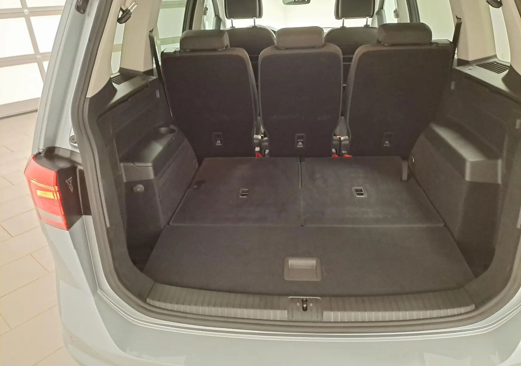 Vue arrière du coffre ouvert du Volkswagen Touran 2025 argent Dolomite, montrant les sièges arrière et l'espace de chargement.
