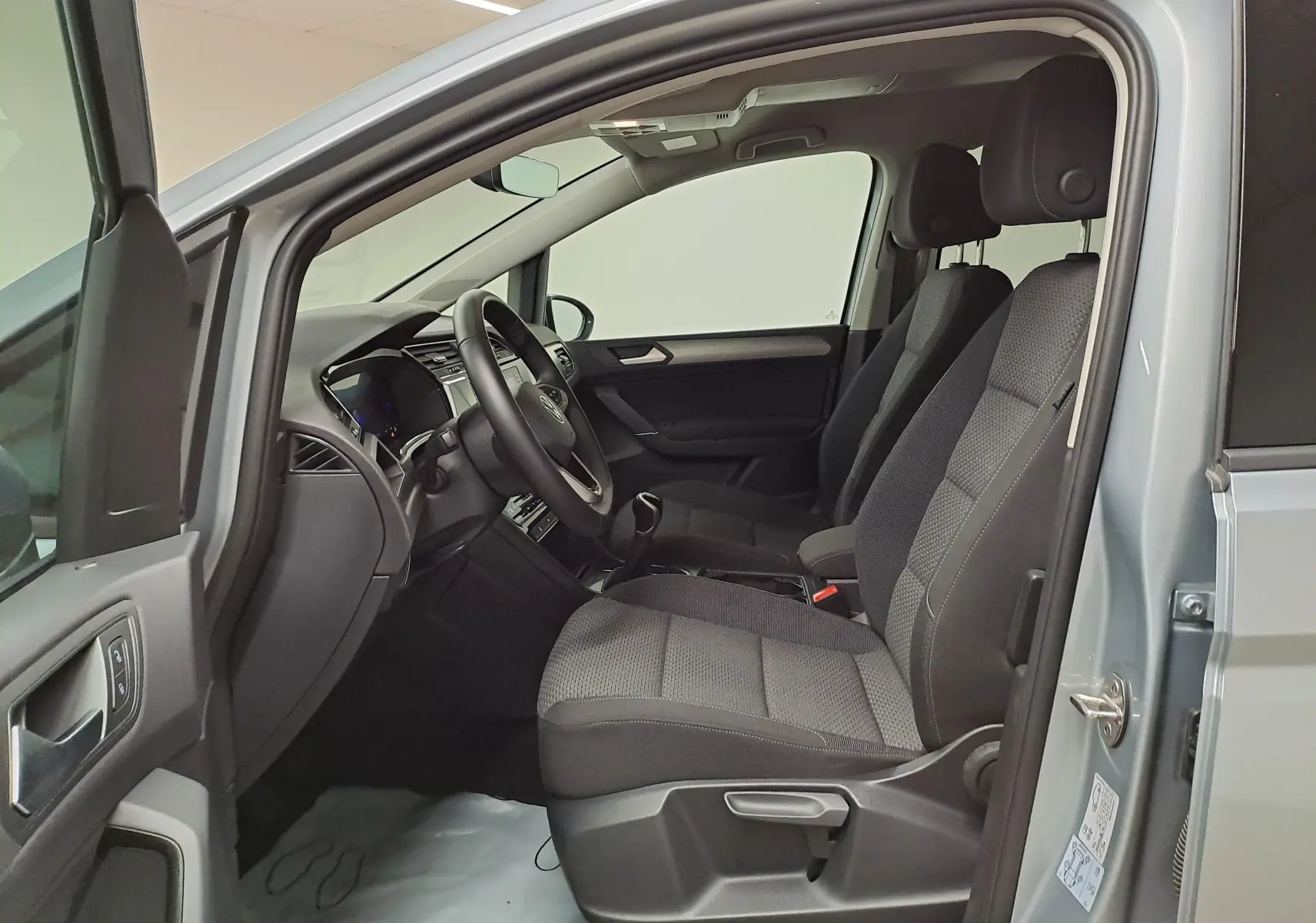 Vue intérieure côté conducteur du Volkswagen Touran 2025 argent Dolomite, montrant les sièges avant et le tableau de bord.