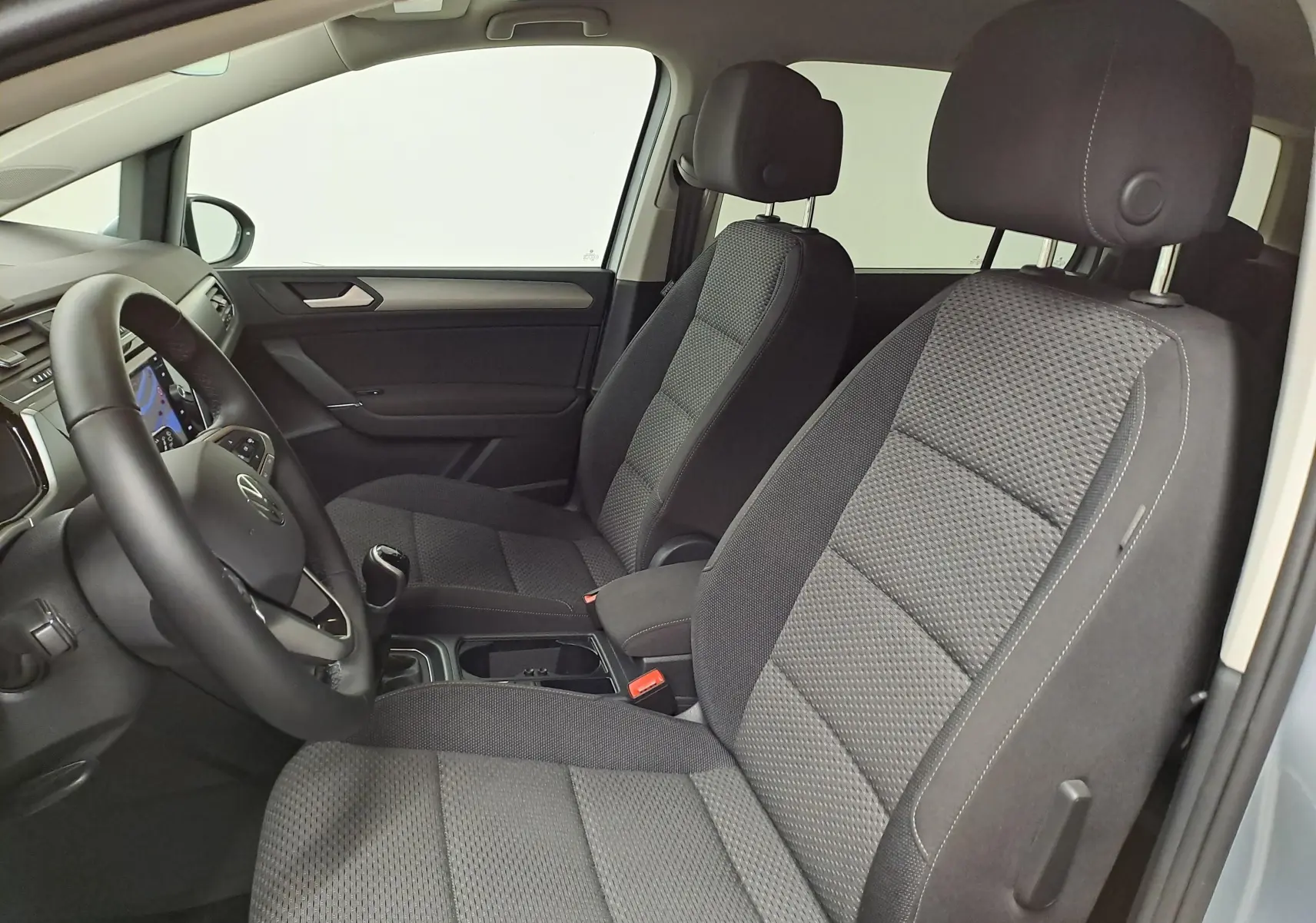 Vue intérieure côté conducteur du Volkswagen Touran 2025 avec sièges tissu gris et volant multifonction noir.