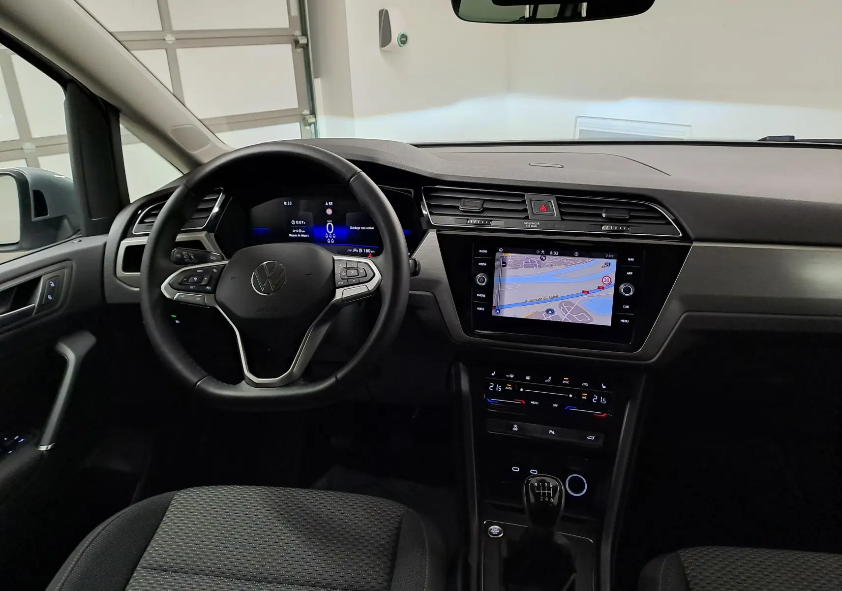 Vue intérieure du Volkswagen Touran 2025 montrant le volant, tableau de bord digital et écran central avec navigation.