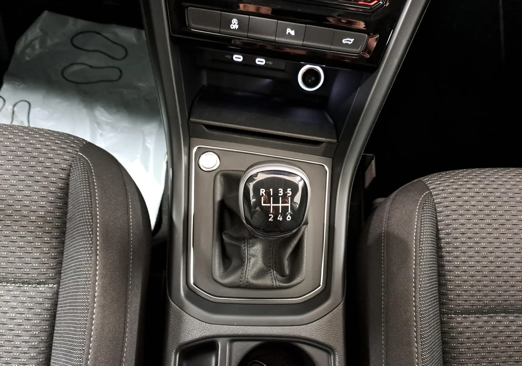Vue rapprochée du levier de vitesses manuel du Volkswagen Touran 2025, entouré des sièges tissu gris.