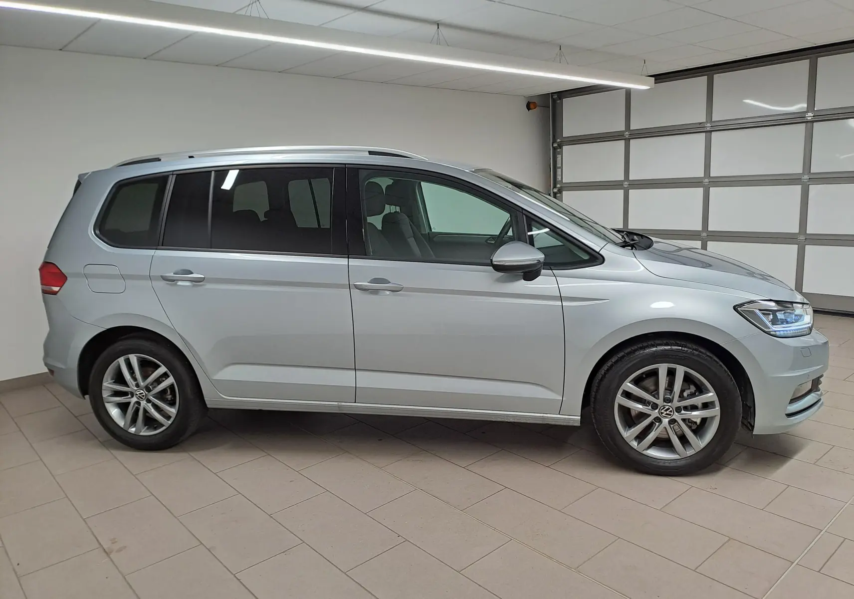 Vue de profil côté gauche d'un Volkswagen Touran 2025 en peinture métallisée Argent Dolomite dans un garage.
