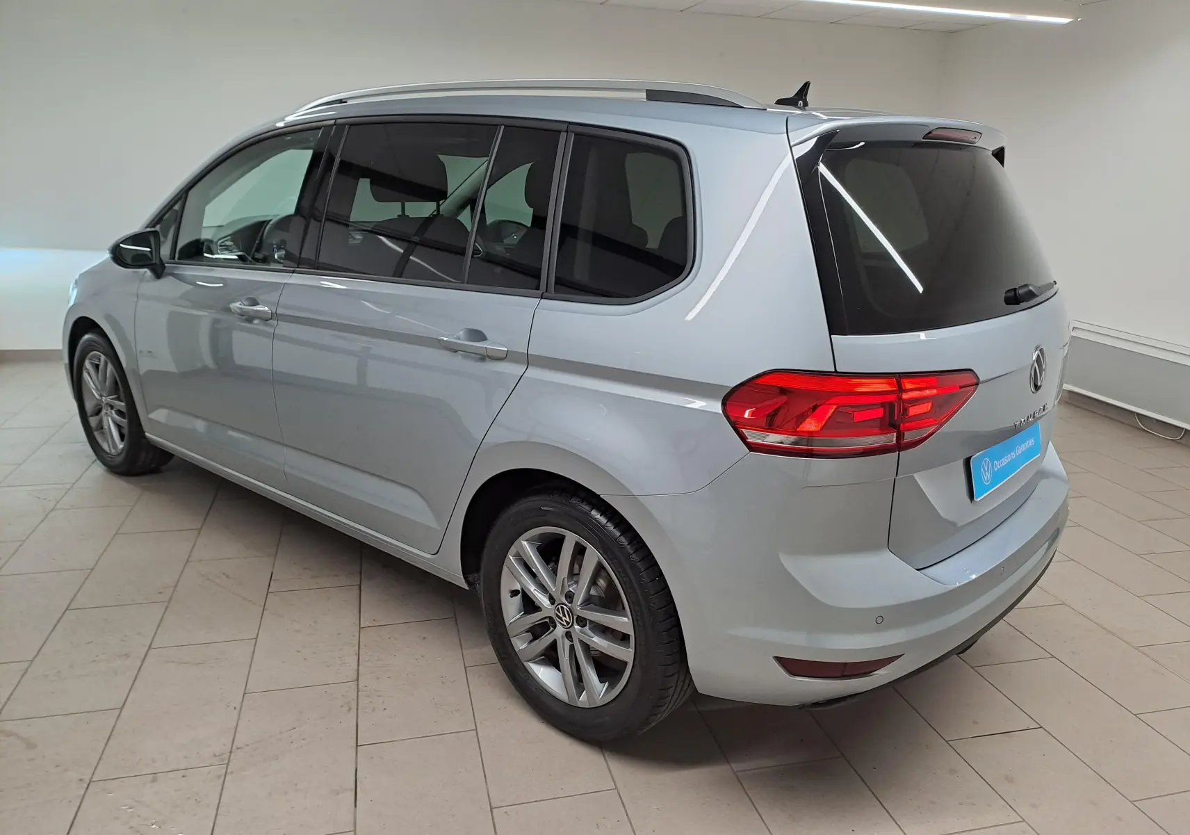 Vue 3/4 arrière gauche d'un Volkswagen Touran 2025 argent Dolomite avec vitres teintées et jantes alliage.