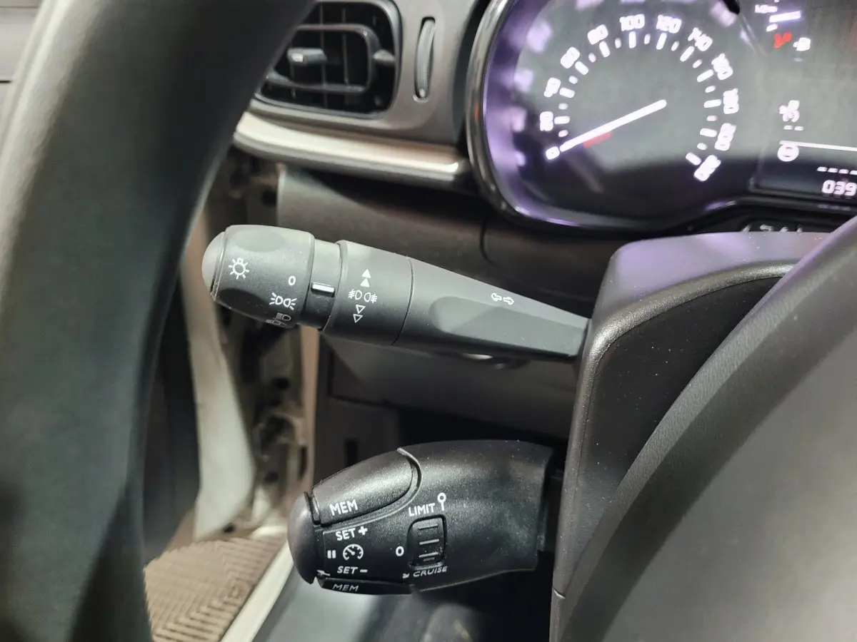 Gros plan sur les commandes au volant de la Citroën C3 beige, avec tableau de bord et indicateur de vitesse partiellement visibles.