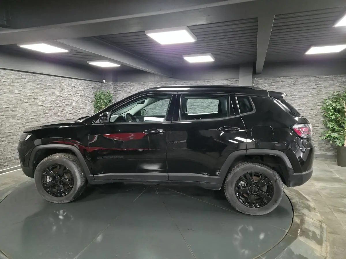 Vue de profil côté gauche d'un Jeep Compass noir avec jantes noires et garde au sol surélevée dans un showroom.