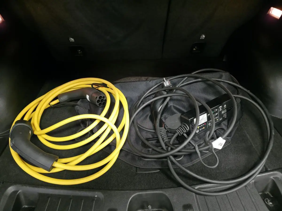 Coffre ouvert d’un Jeep Compass noir 2024 montrant deux câbles de recharge pour hybride rechargeable.