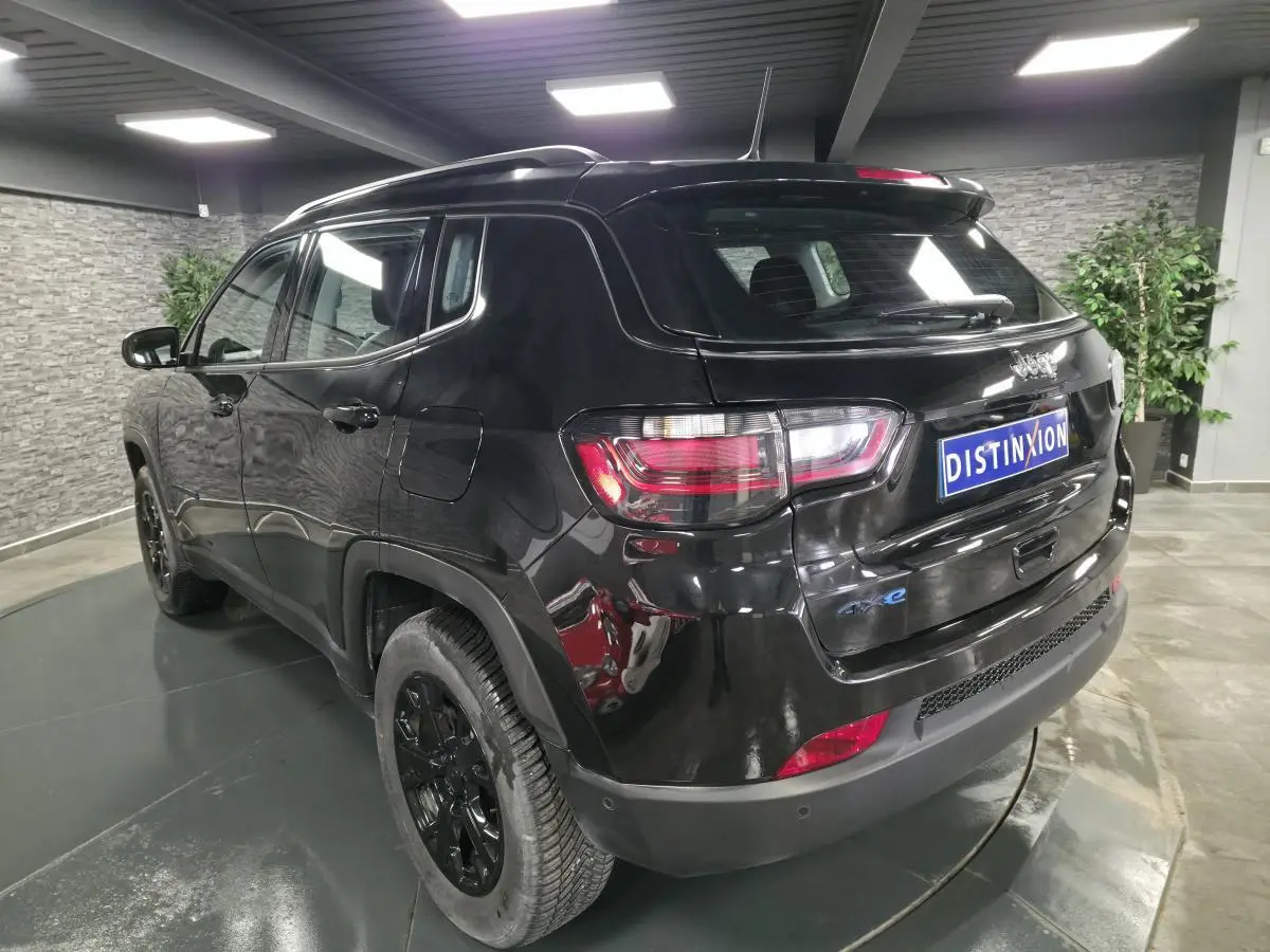 Vue 3/4 arrière droite du Jeep Compass noir brillant avec jantes noires et feux arrière LED en intérieur showroom.