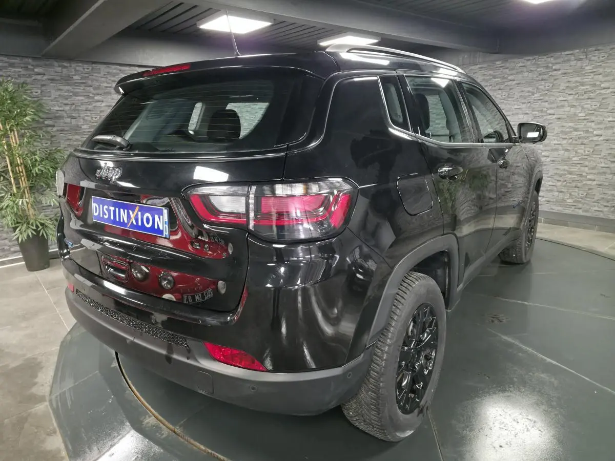 Vue 3/4 arrière droite d'un Jeep Compass noir brillant avec jantes noires et feux arrière LED dans un showroom.