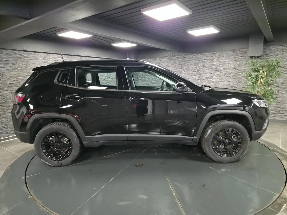 Jeep Compass noir vue de profil côté gauche, avec jantes alliage noires et garde au sol surélevée dans un showroom.