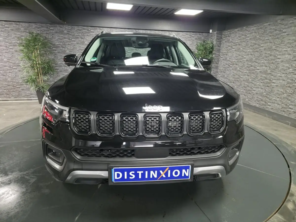 Vue avant d'un Jeep Compass noir 2024 avec calandre distinctive et plaque Distinxion en intérieur showroom.