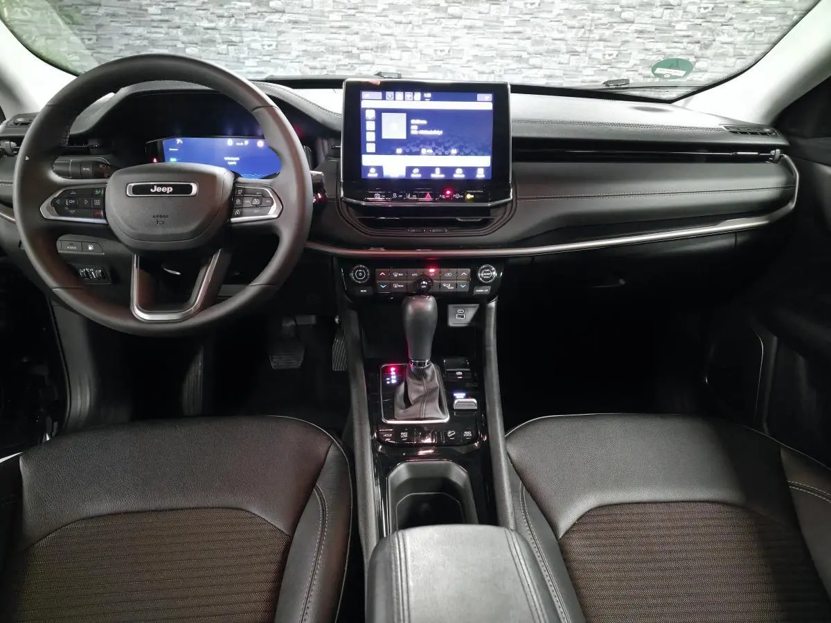 Vue intérieure avant du Jeep Compass 2024 noir, avec tableau de bord numérique et écran tactile central lumineux.