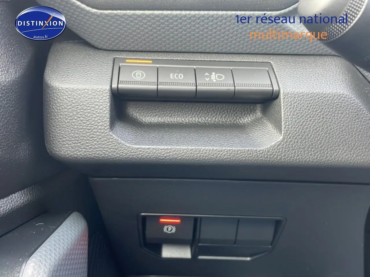 Gros plan sur les commandes du tableau de bord côté gauche du Dacia Duster vert cèdre, avec bouton Eco et frein à main électronique.