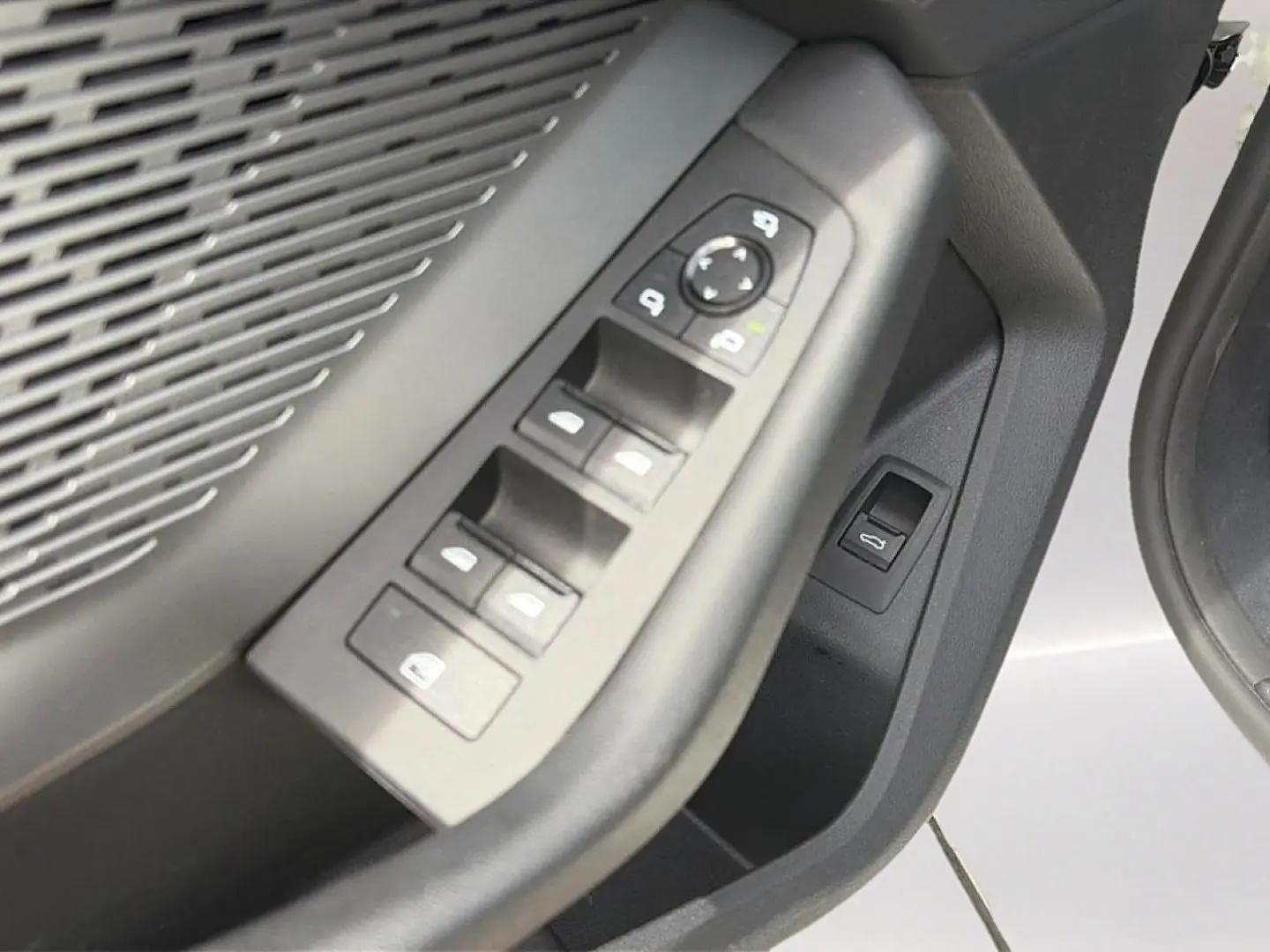 Gros plan sur les commandes des vitres et rétroviseurs côté conducteur d'une BMW Série 1 blanche.
