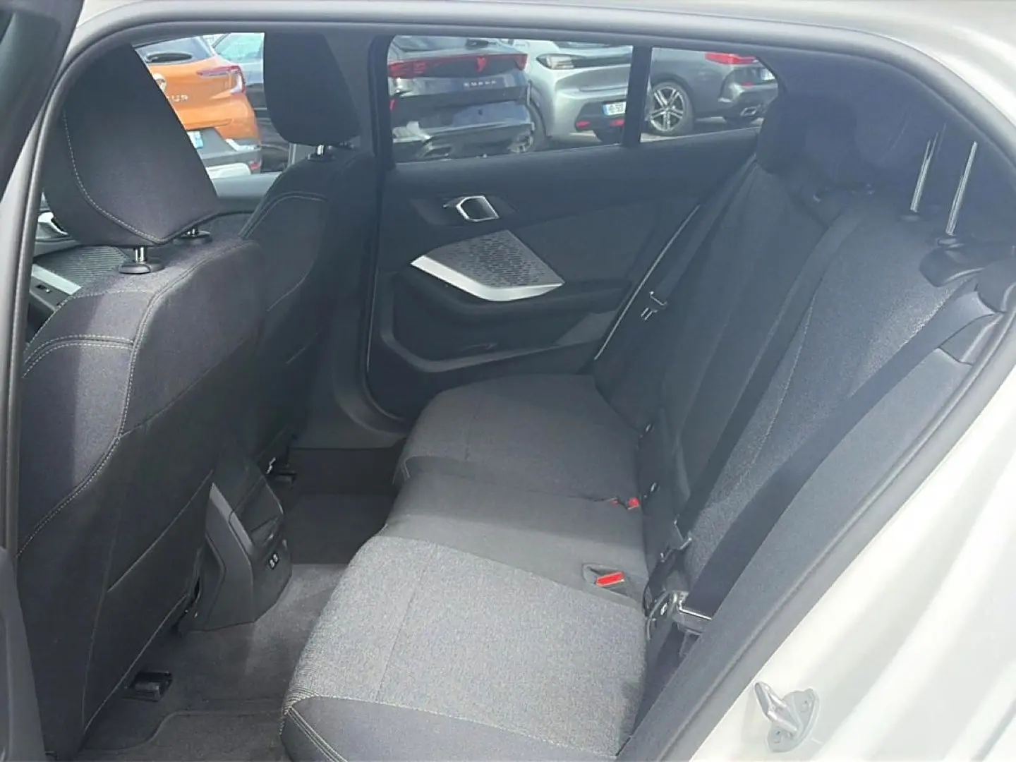 Vue intérieure arrière côté droit de la BMW Série 1 blanche, montrant la banquette tissu gris et la portière ouverte.
