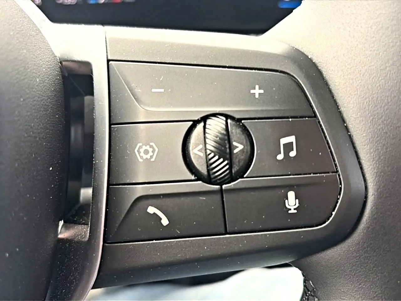 Gros plan sur les commandes noires multifonctions au volant côté gauche de la BMW Série 1 blanche 2025.