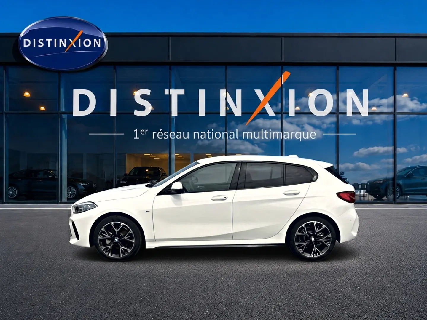 BMW Série 1 blanche vue de profil côté gauche, avec jantes alliage noires et vitres teintées, devant une vitrine Distinxion.