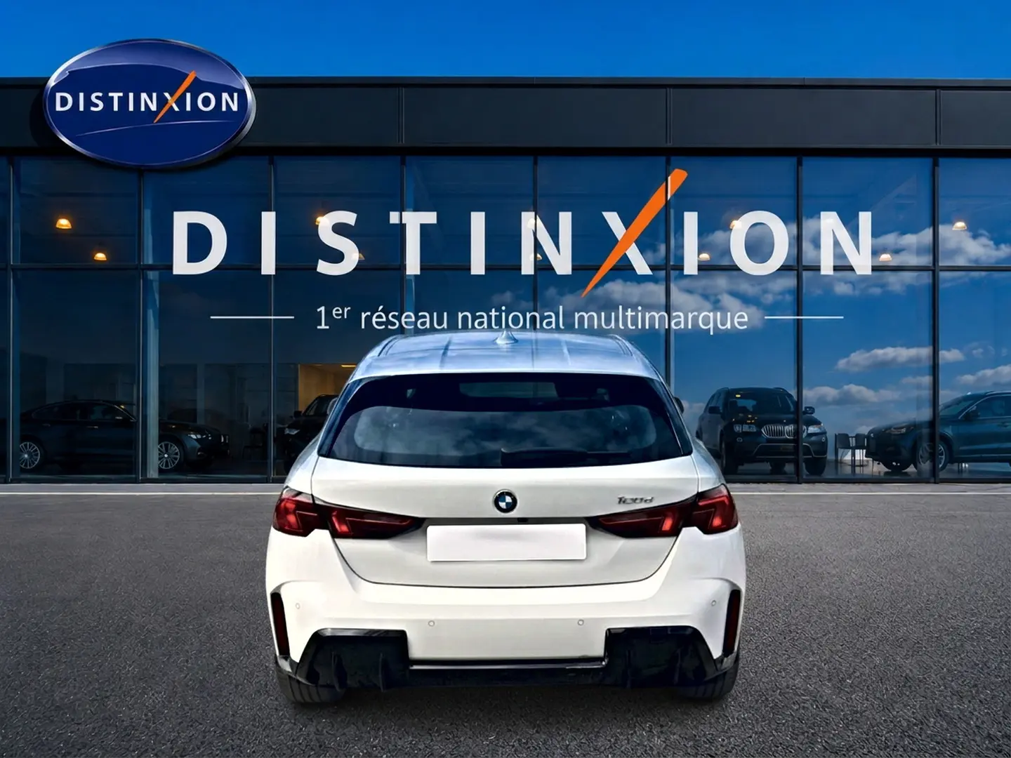 Vue arrière d'une BMW Série 1 blanche pure (120da M Sport) garée devant une vitrine avec logo Distinxion.