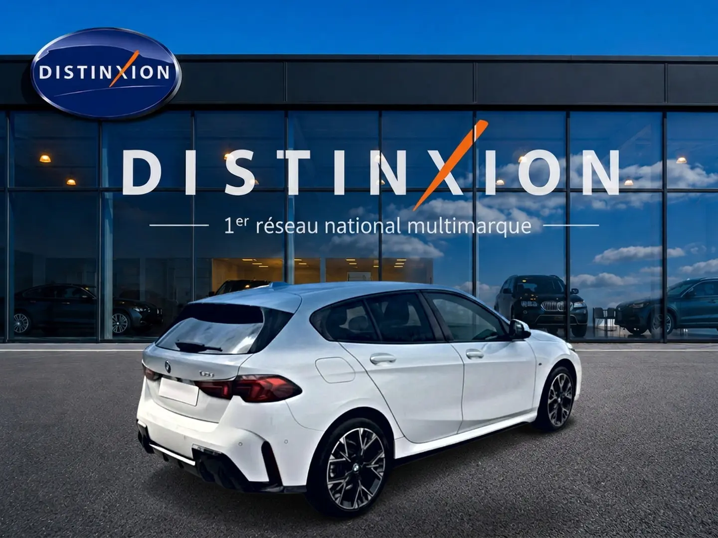 BMW Série 1 blanche vue en 3/4 arrière droit, avec jantes sport et feux arrière LED sombres, devant une vitrine Distinxion.