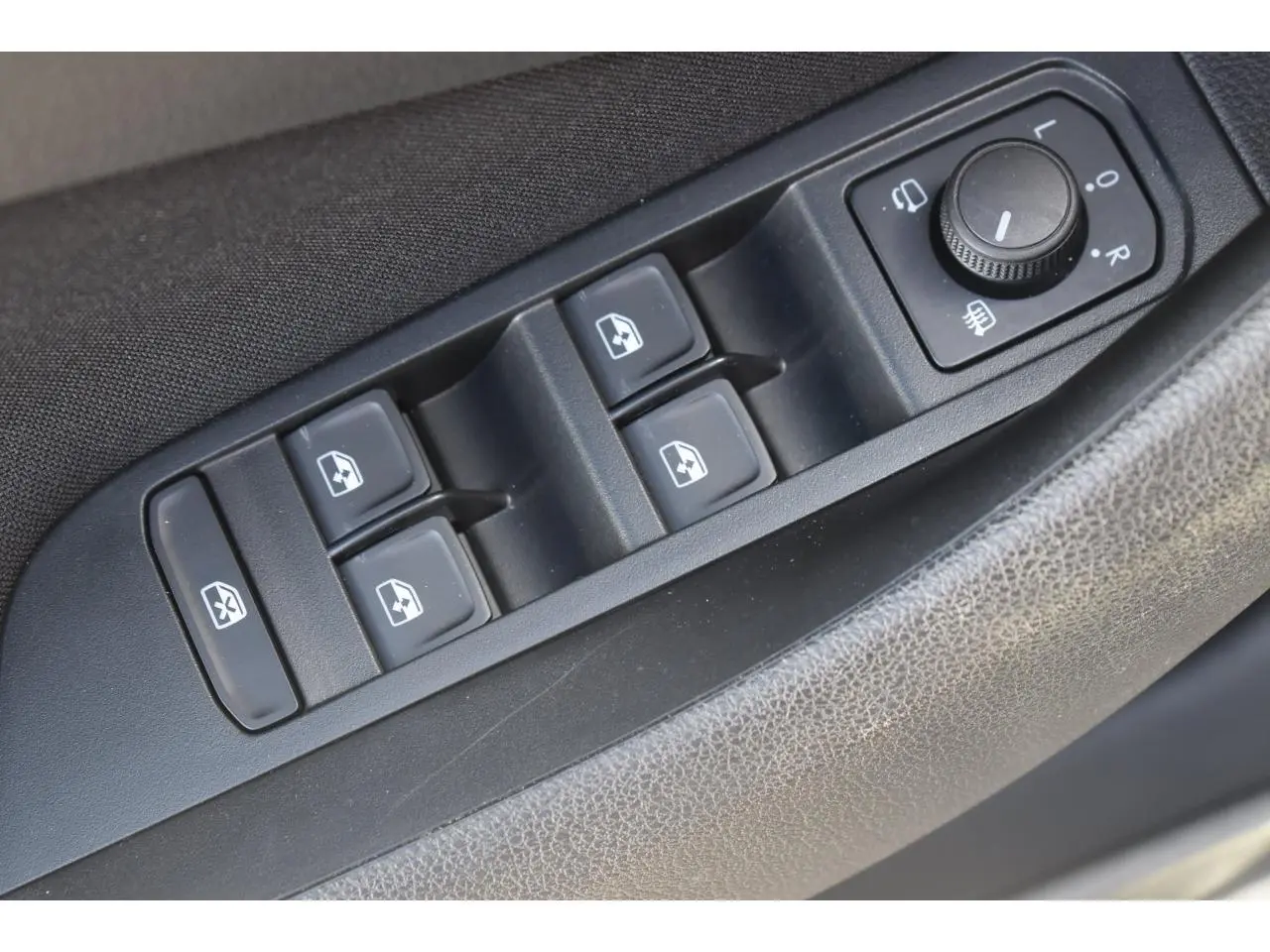 Gros plan sur les commandes de lève-vitres et réglage des rétroviseurs côté conducteur d'une Skoda Scala gris graphite.