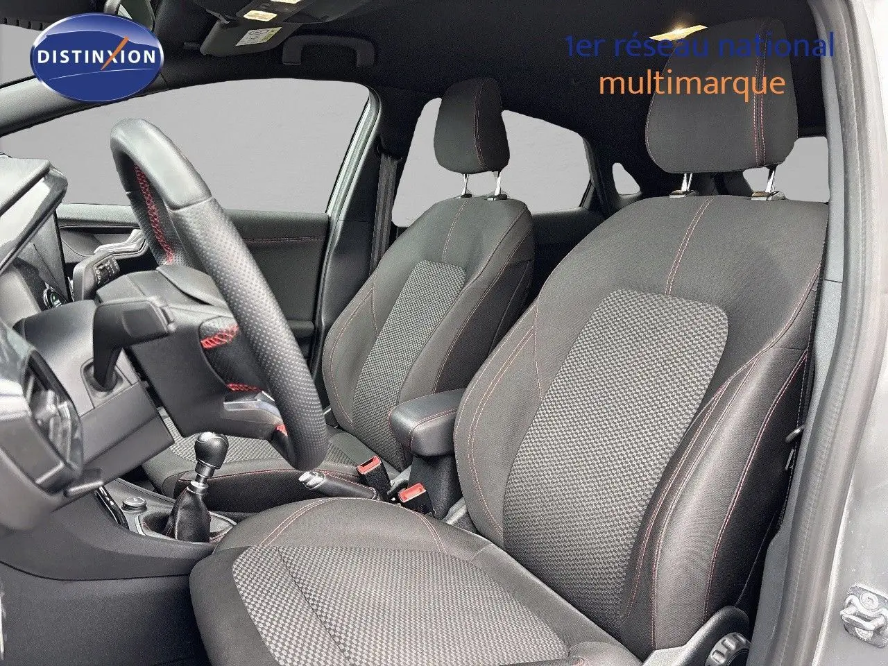 Intérieur avant du Ford Puma gris Solar, sièges noirs avec surpiqûres rouges et volant cuir perforé en vue latérale droite.