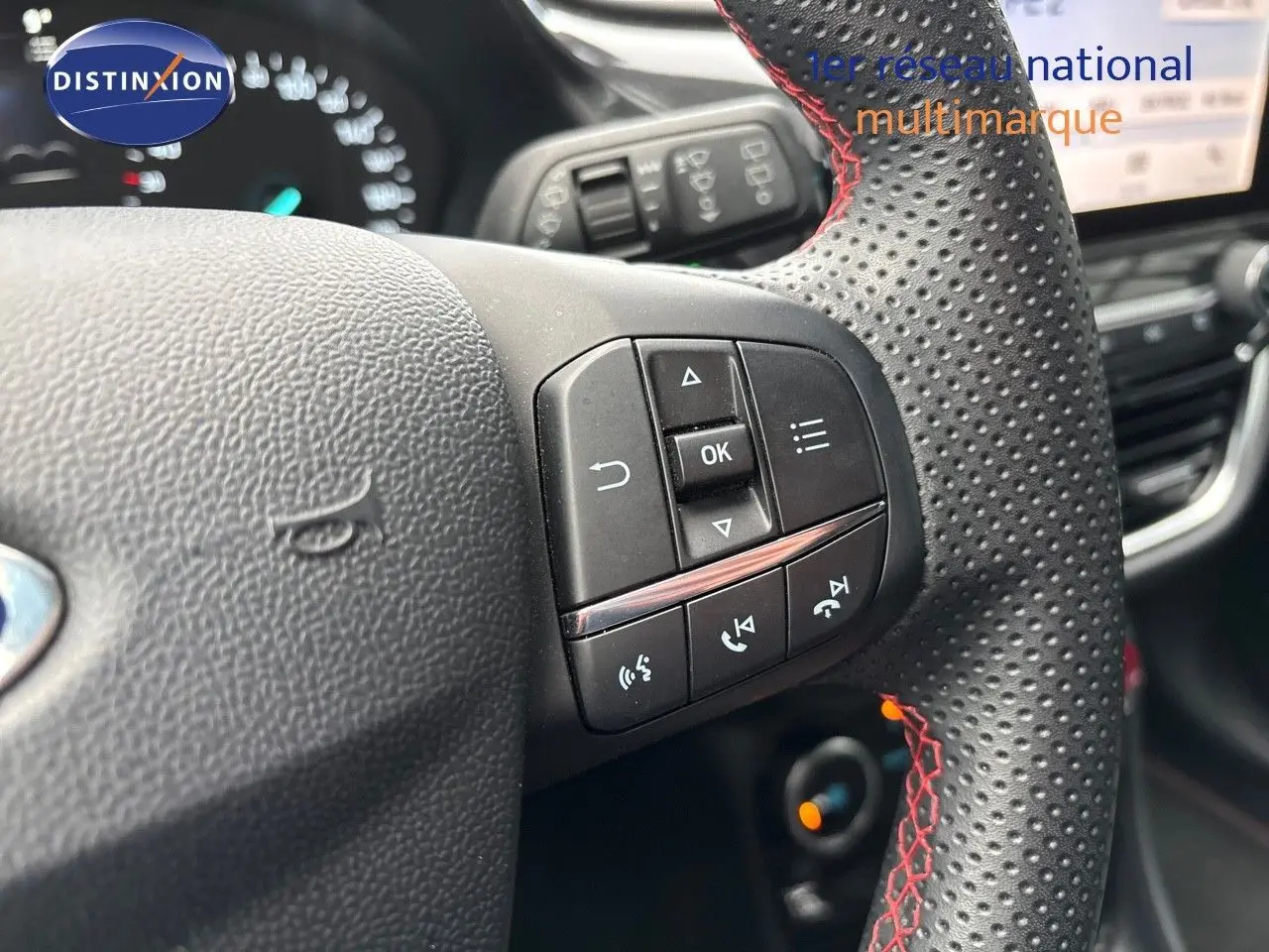 Gros plan sur le volant perforé avec surpiqûres rouges du Ford Puma gris Solar, montrant les commandes multifonctions.