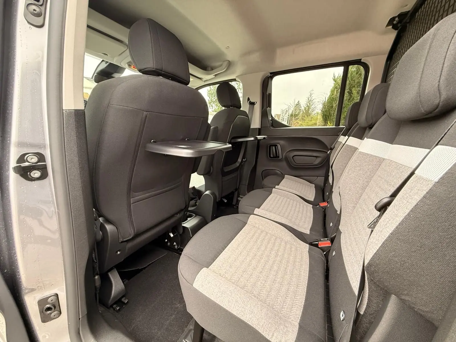 Vue intérieure côté droit du Citroën Berlingo gris Artense 2025, montrant les sièges arrière avec tablette rabattable.