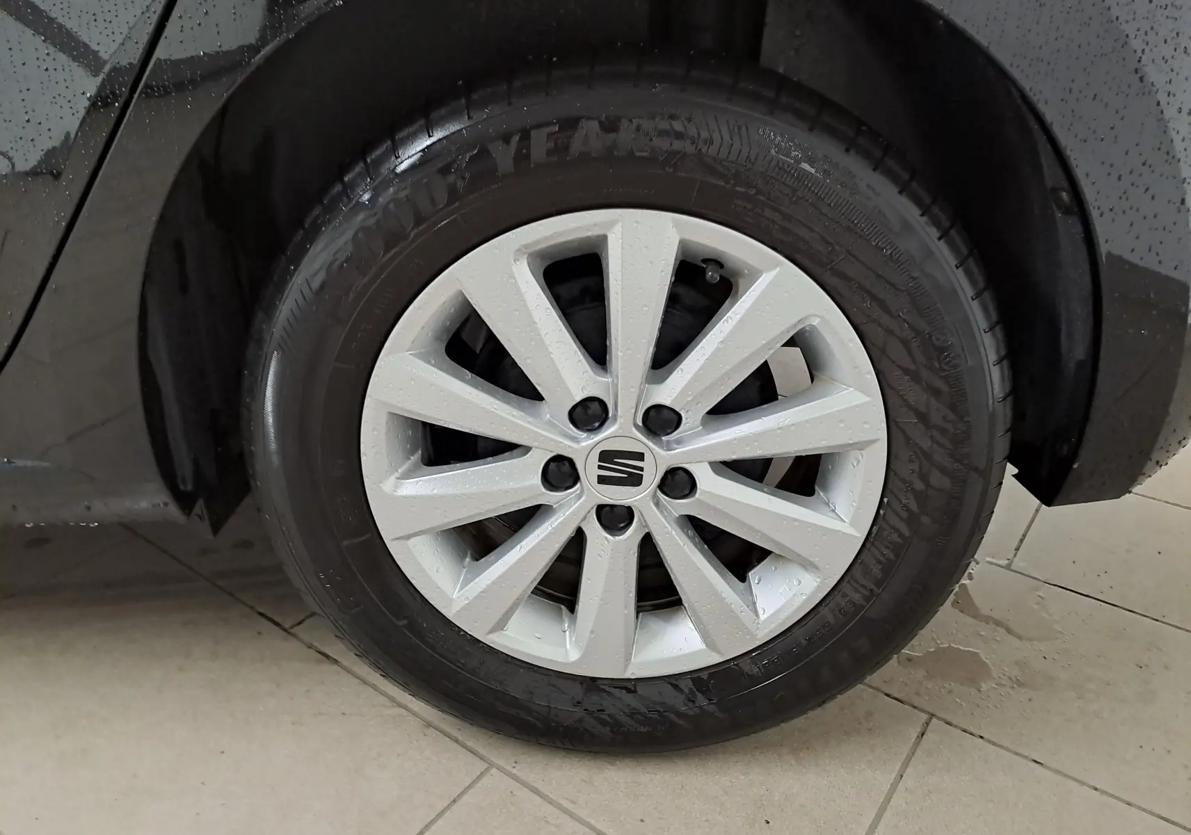 Gros plan sur la jante alliage 15'' Enjoy argentée de la SEAT Ibiza noir minuit, côté arrière droit sous la pluie.
