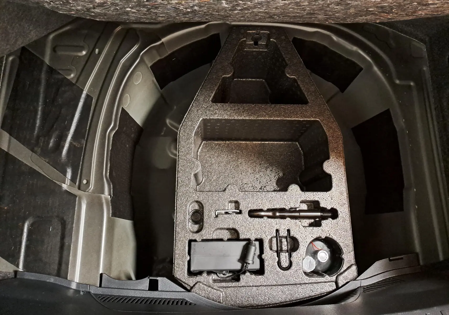 Vue plongeante sur le coffre ouvert d'une SEAT Ibiza 2024 noir minuit, montrant le rangement pour roue de secours et outils.