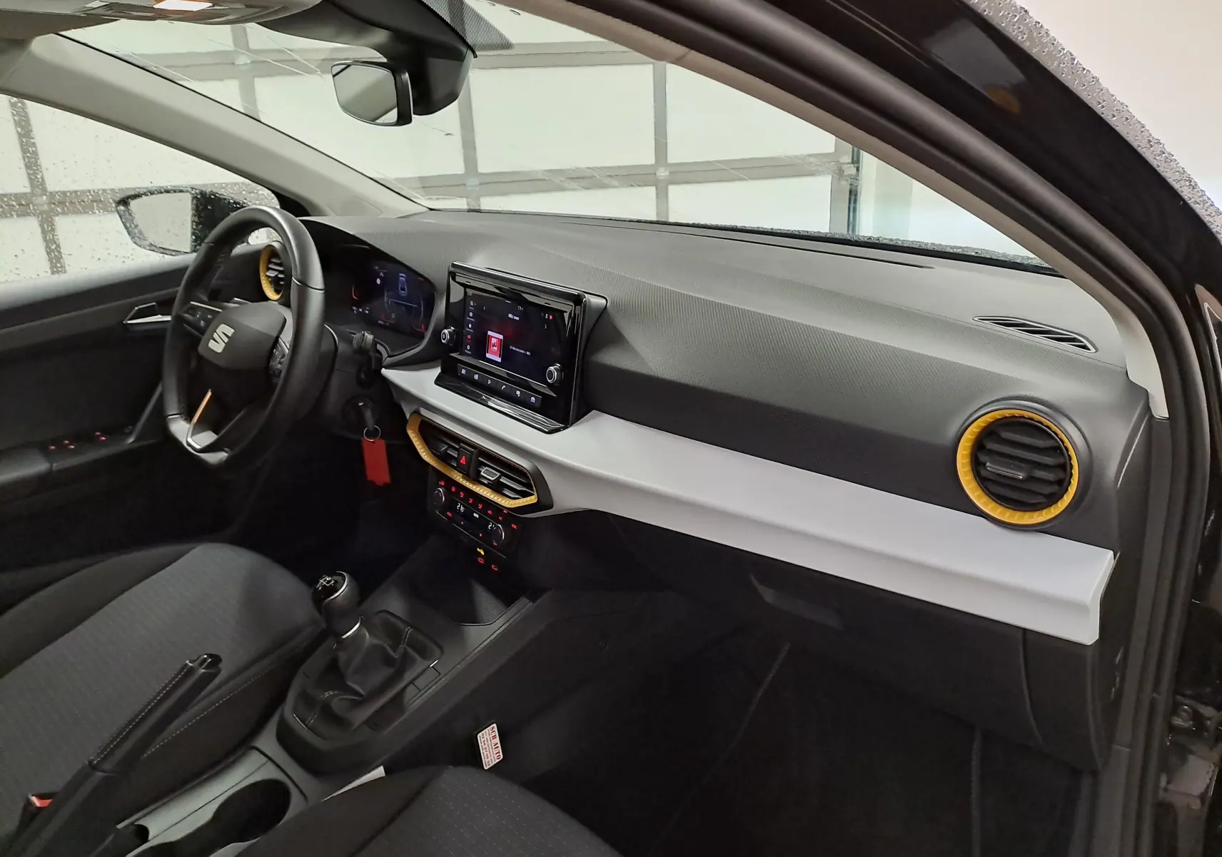 Vue intérieure côté conducteur de la SEAT Ibiza noire, avec tableau de bord gris clair et aérateurs cerclés de jaune.