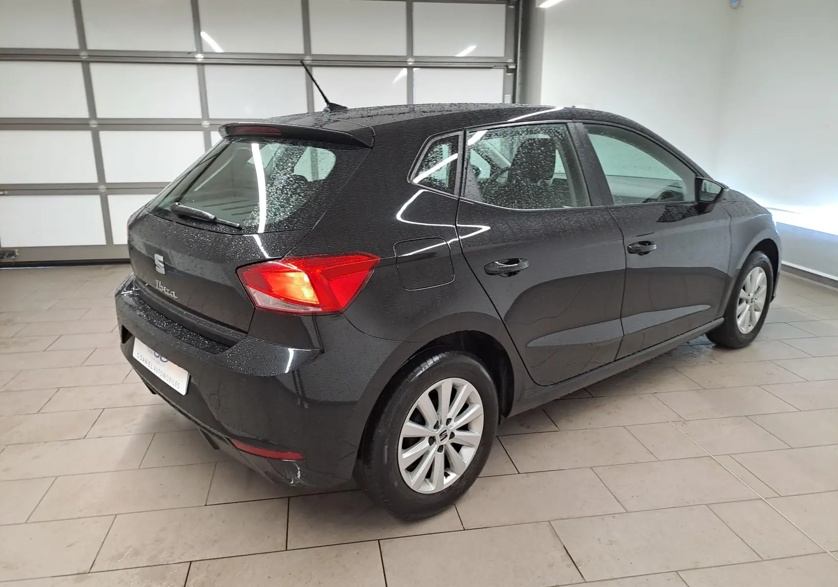 Vue 3/4 arrière droite d'une SEAT Ibiza noire minuit avec jantes alliage 15'' dans un garage lumineux.