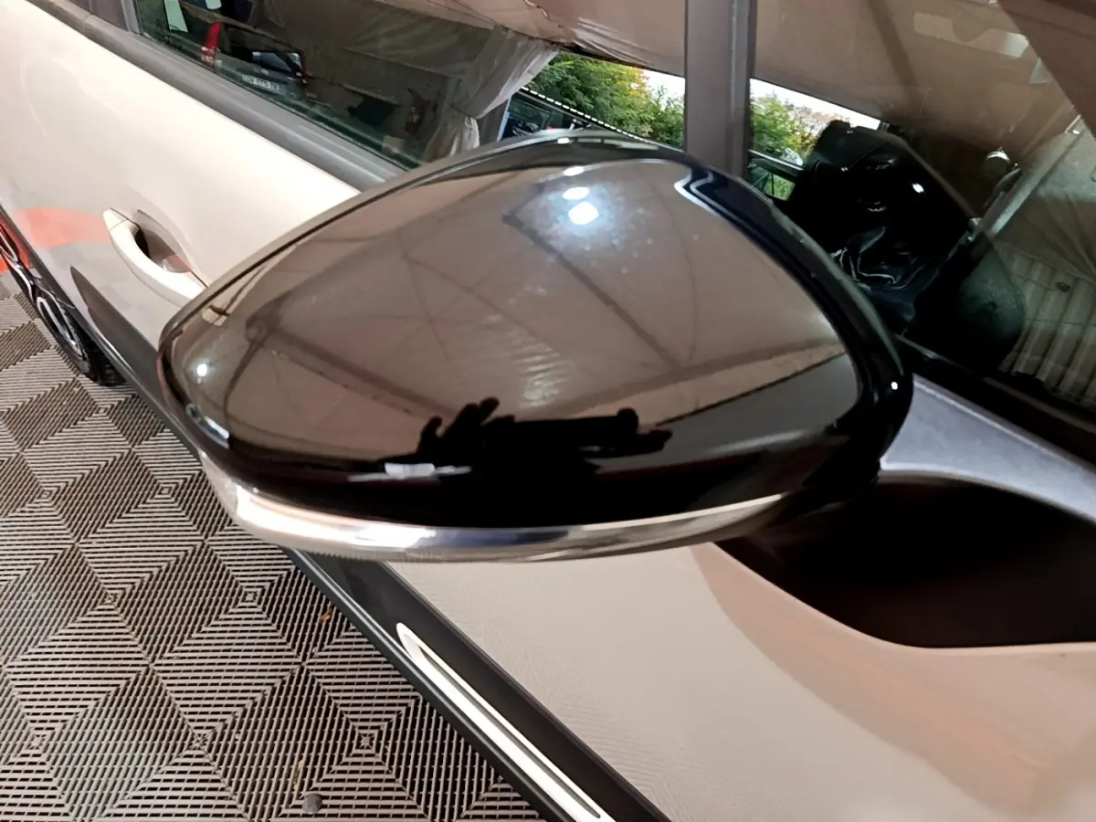 Rétroviseur noir brillant côté conducteur d'une Citroën C3 beige vue de près, avec poignée de porte visible.