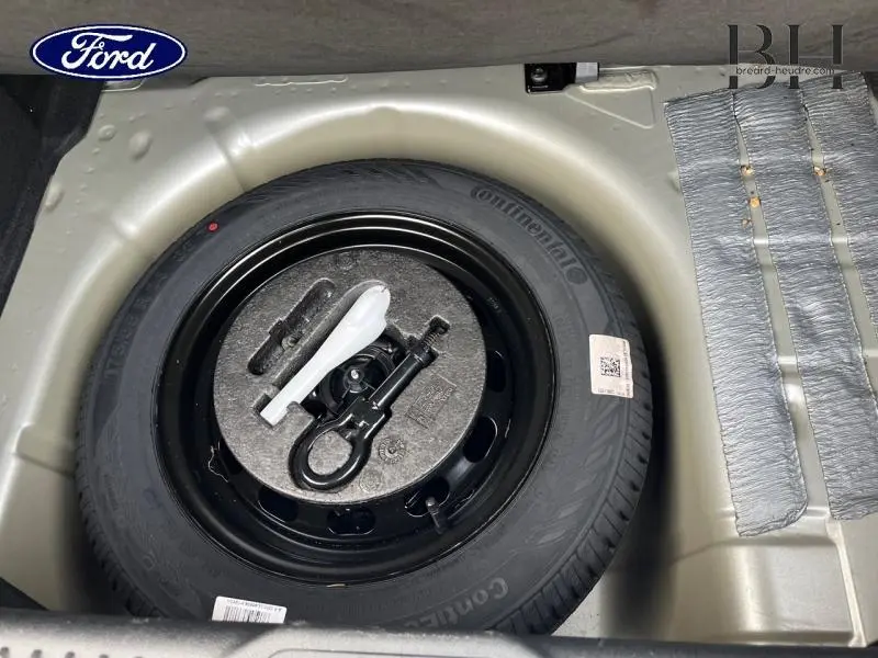 Vue rapprochée de la roue de secours noire dans le coffre d'une Ford Fiesta 2020 gris lunaire, avec outils de dépannage intégrés.