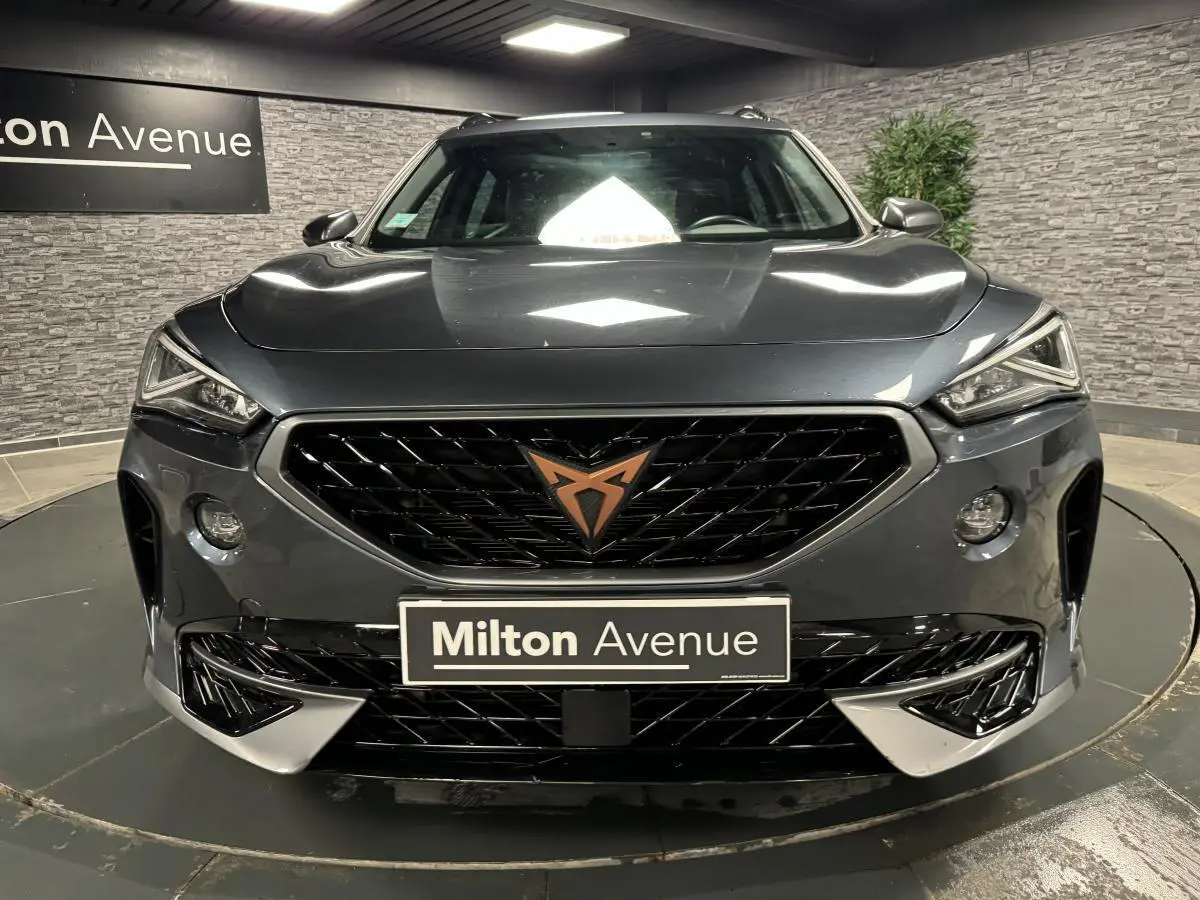 Vue frontale d'un CUPRA Formentor gris magnétique avec calandre noire et logo cuivre, dans un showroom intérieur.