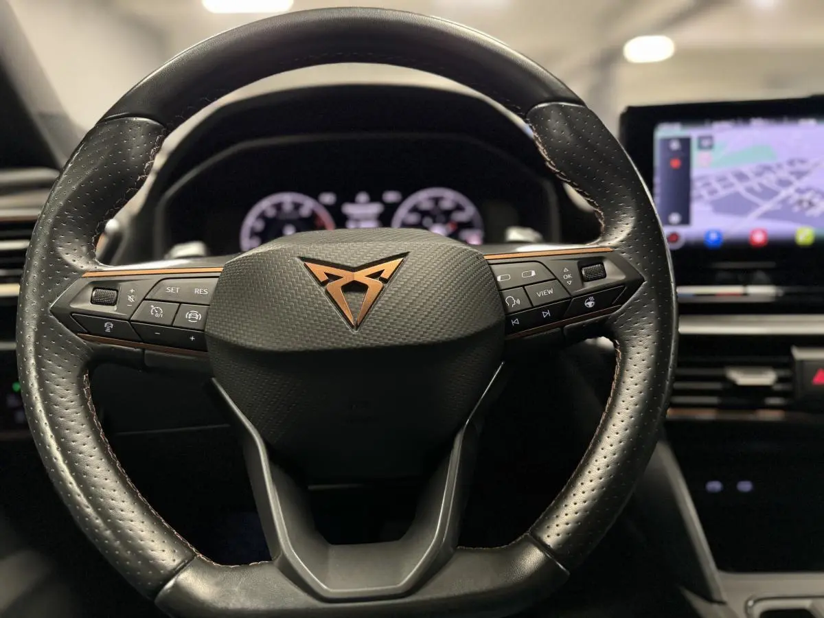 Volant sport noir avec logo CUPRA cuivre au centre, vue frontale sur le tableau de bord digital et écran tactile GPS.
