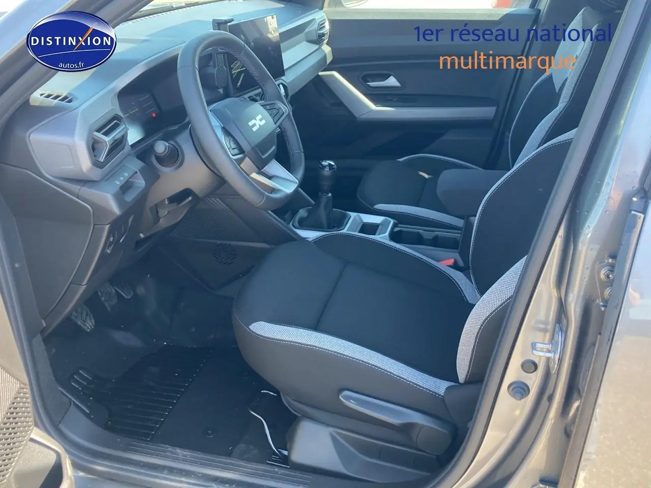 Vue intérieure côté conducteur du Dacia Duster gris schiste 2026, avec volant multifonction et siège tissu noir et gris.