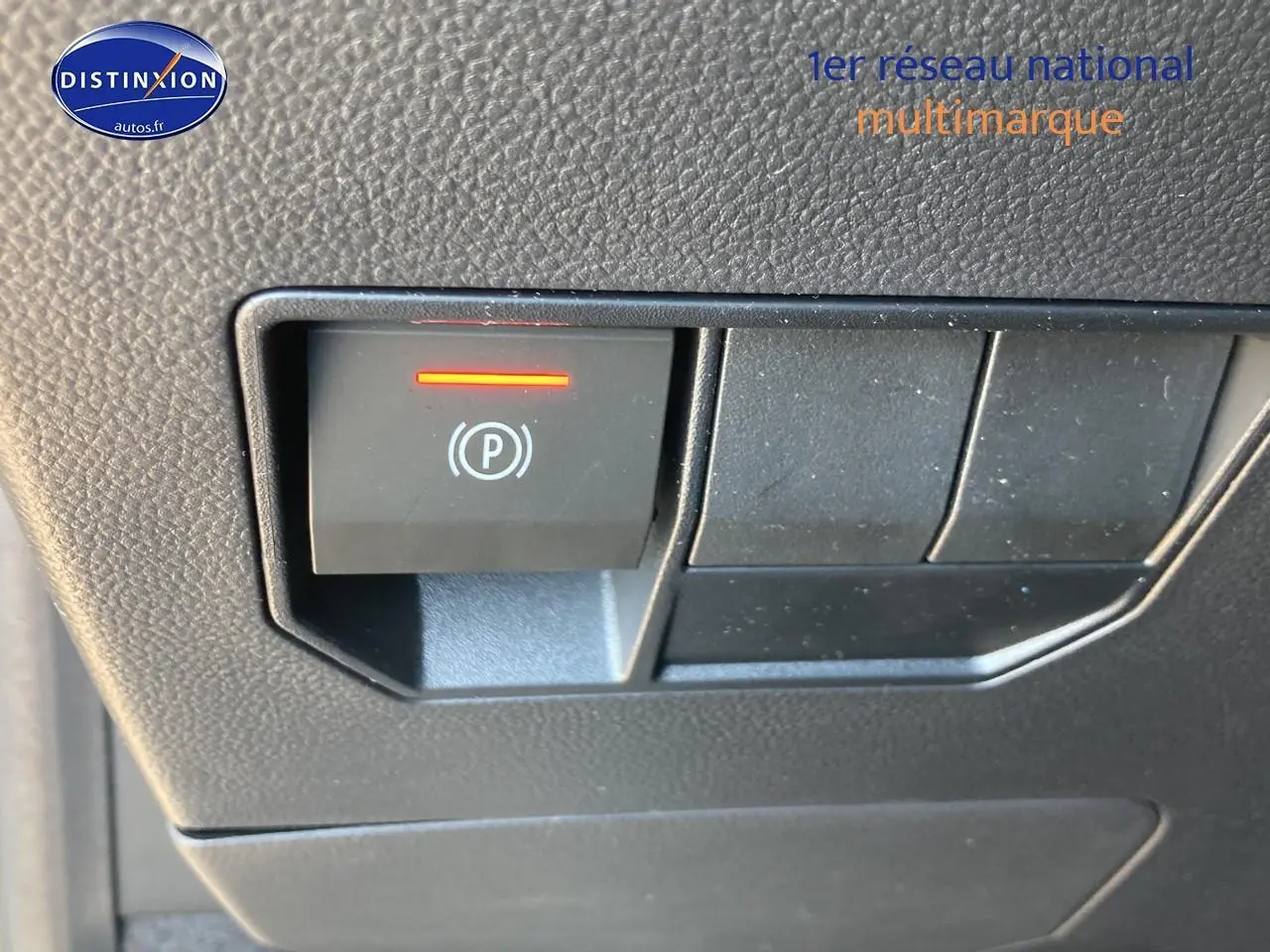 Gros plan sur le bouton de frein de stationnement électrique allumé dans l'habitacle du Dacia Duster gris schiste.