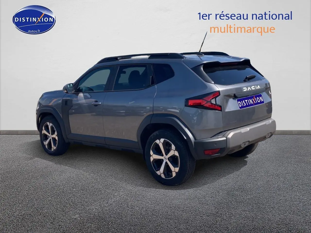 Vue 3/4 arrière droite d'un Dacia Duster gris schiste avec barres de toit et jantes alu distinctives.