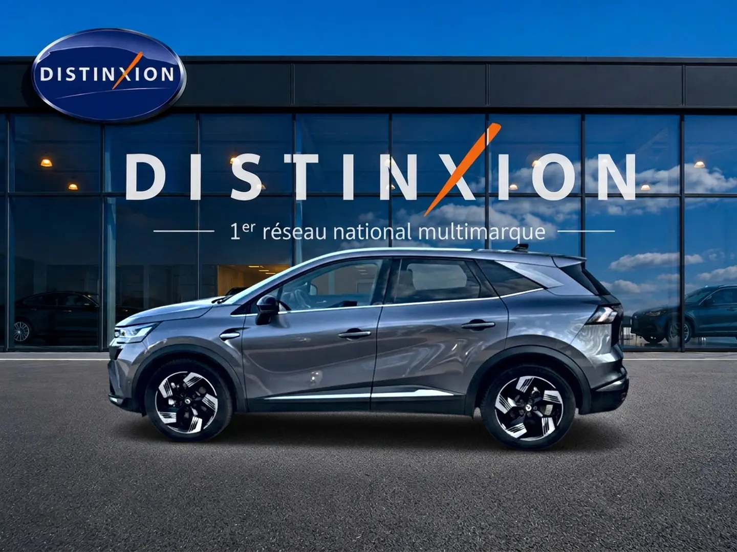 Profil droit d’un Renault Symbioz gris cassiopée 2025 devant une vitrine avec logo Distinxion.