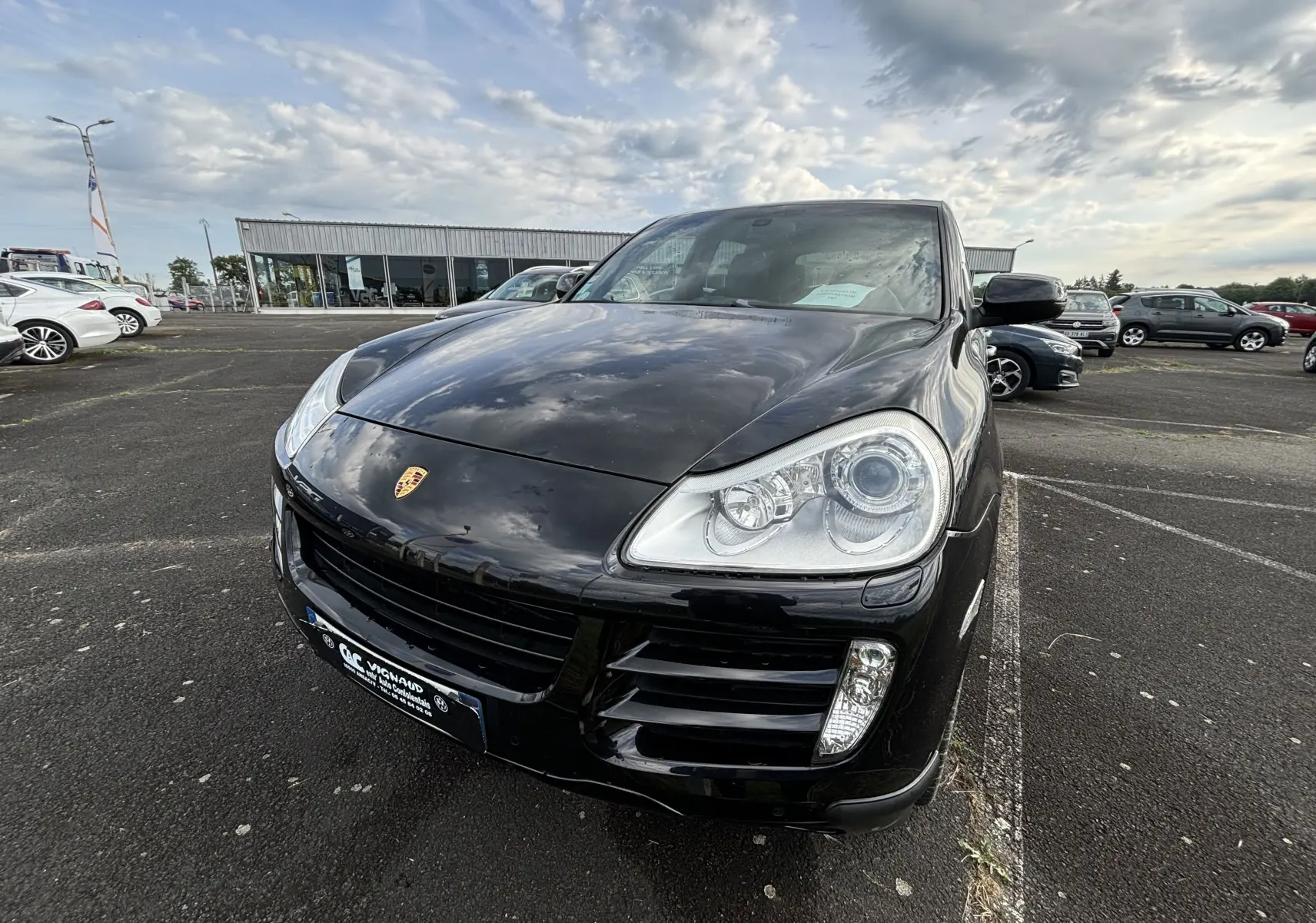 Vue 3/4 avant d'un Porsche Cayenne S noir brillant, mettant en valeur ses phares distinctifs et son logo Porsche sur le capot.