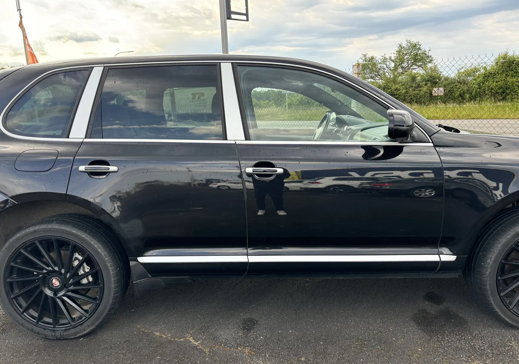 Profil côté gauche d'un Porsche Cayenne noir 2007 avec jantes noires et finitions chromées sur les portières.
