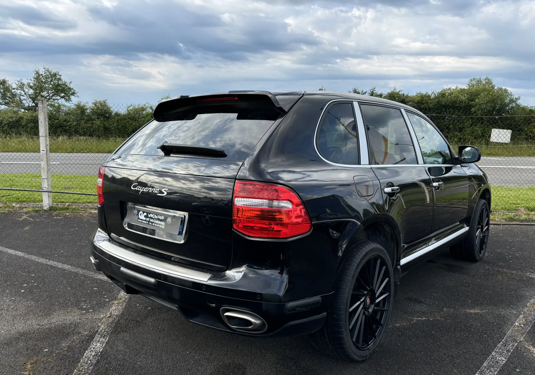 Vue 3/4 arrière droite d'un Porsche Cayenne S noir de 2007 avec jantes noires et feux arrière rouges.