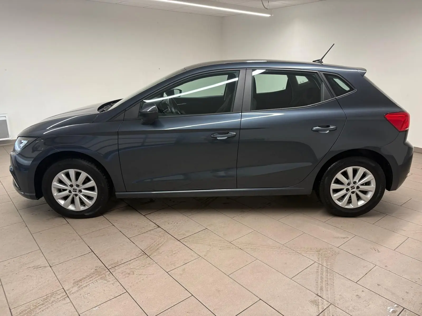 Vue de profil côté gauche d'une SEAT Ibiza 2024 gris magnétique, compacte et élégante, stationnée en intérieur.