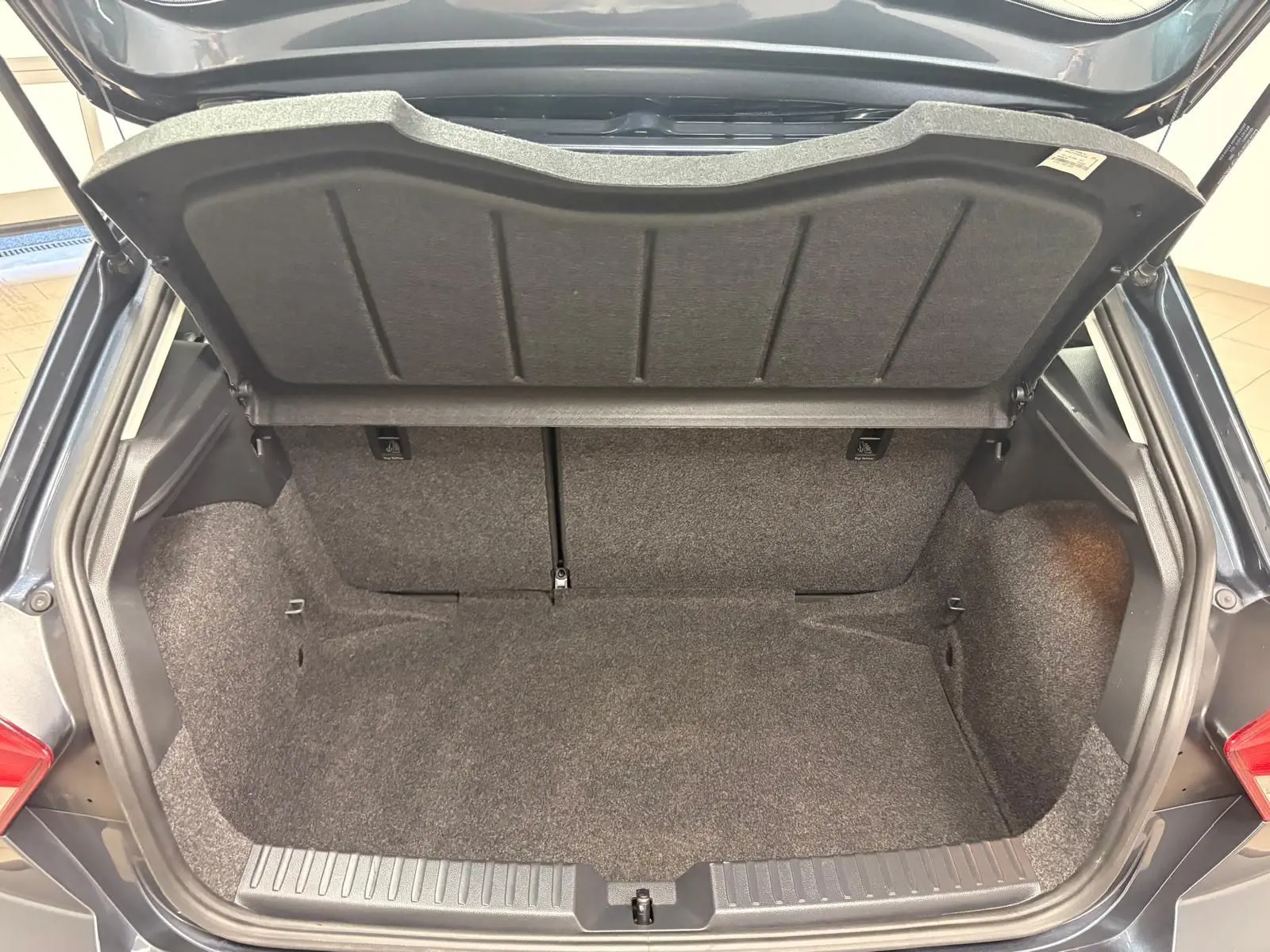 Coffre ouvert de la SEAT Ibiza 2024 gris magnétique, vue arrière montrant l’espace de rangement vide et la moquette intérieure.