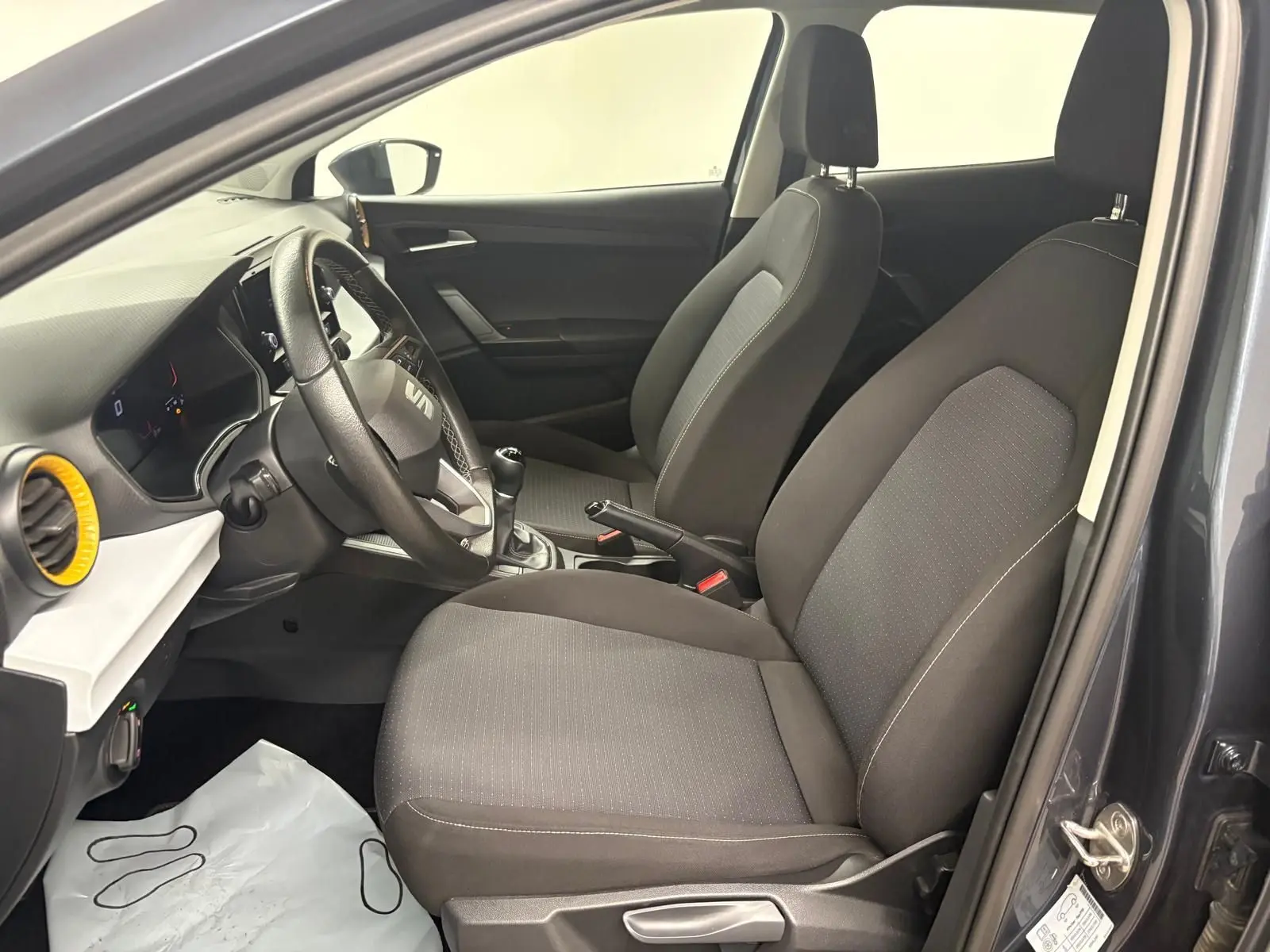 Intérieur avant droit de la SEAT Ibiza 2024 gris magnétique, montrant sièges tissu, volant et levier de vitesses manuel.