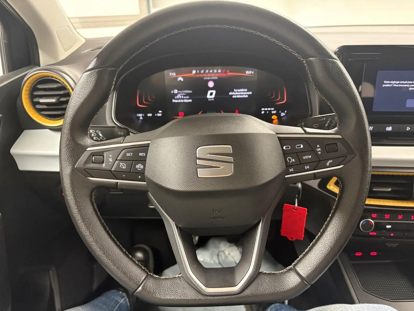 Vue intérieure centrée sur le volant cuir de la SEAT Ibiza 2024 gris magnétique avec tableau de bord numérique et aérateurs jaunes.